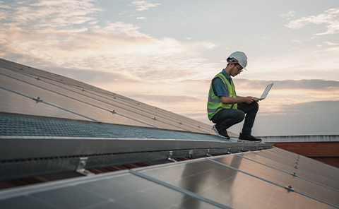 a man in a reflective vest and hardhat on a roof with a laptop